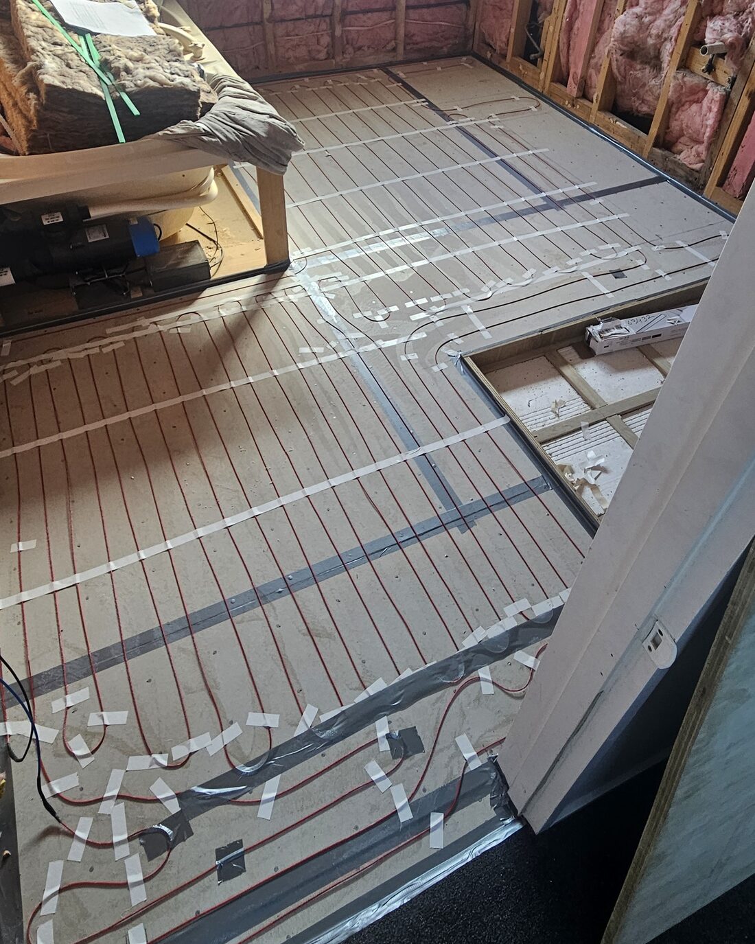 Underfloor heating cable laid out across a stripped bathroom floor, taped and ready for the screed