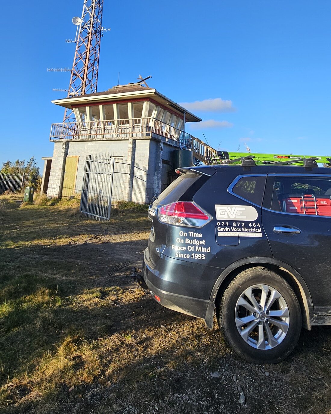 The signwritten Gavin Voss Electrical wagon parked below a transmitter mast